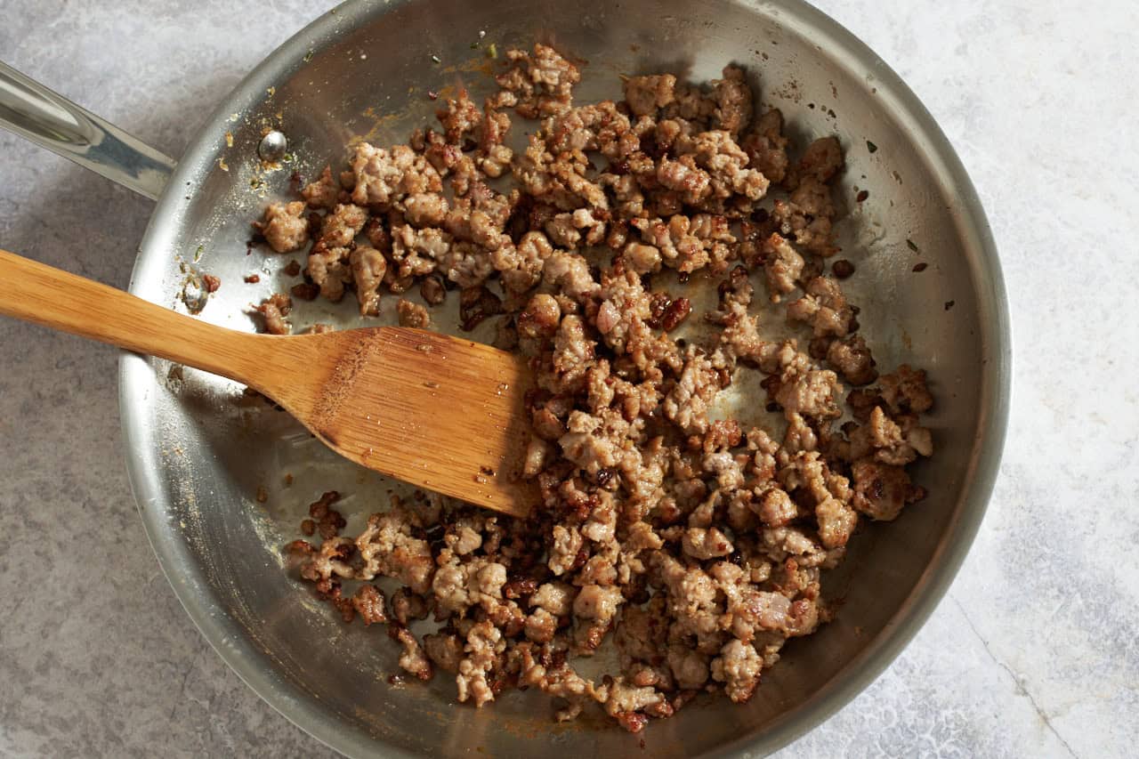 Browned Italian sausage in a skillet with a bamboo spatula.