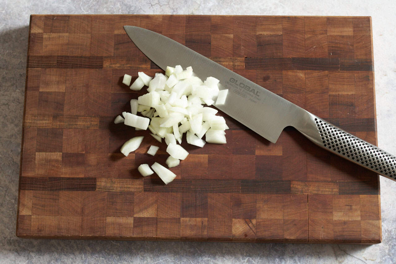 A knife on a cutting board with diced onions.