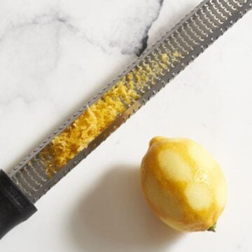 A microplane grater with lemon zest next to a lemon that has been zested.