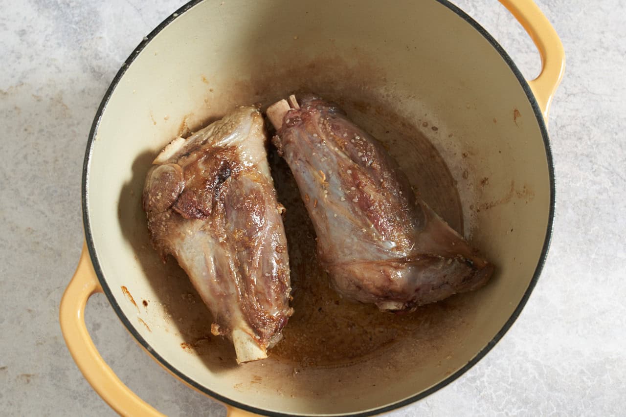 Two seared lamb shanks in a dutch oven.