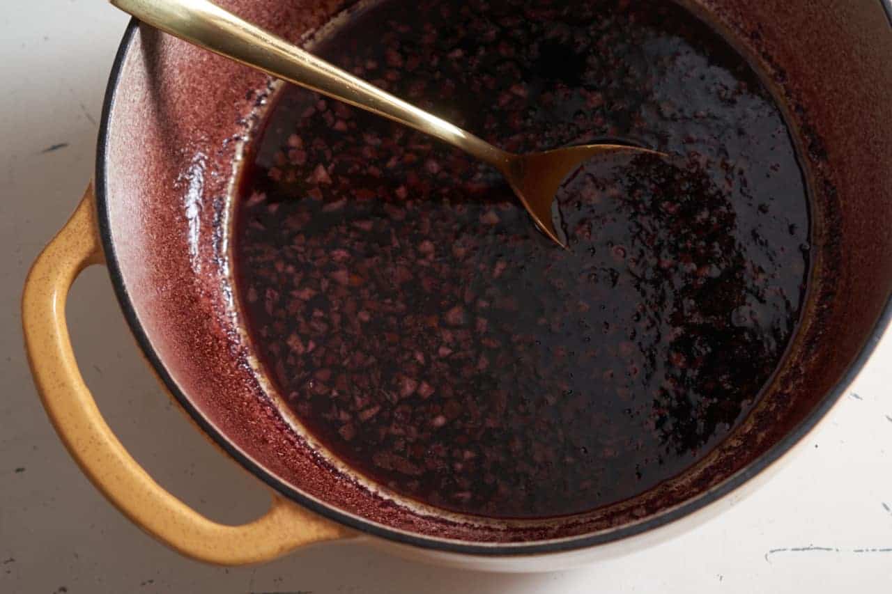 A gold spoon in a pot of red wine sauce.