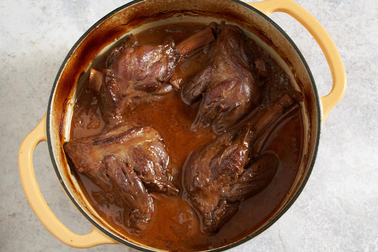 A yellow dutch oven with Red wine braised lamb shanks in a reduced sauce after cooking.