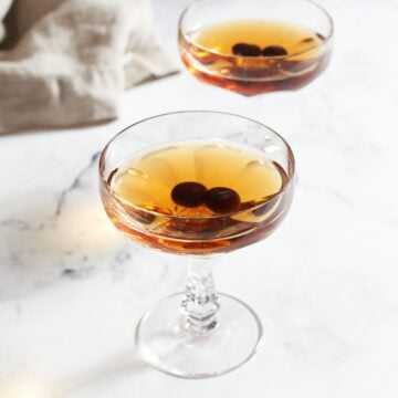 Two maple manhattan drinks in coupe glasses with cocktail cherries.