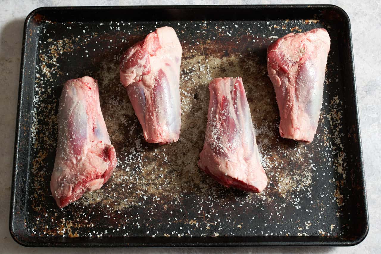 Lamb shanks on a sheet pan seasoned with salt and pepper.