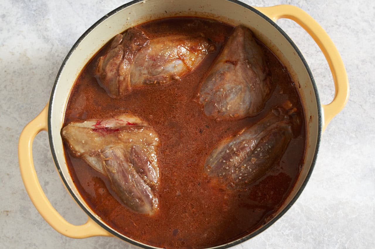 Lamb shanks in red wine braising liquid in a dutch oven, ready to be cooked.