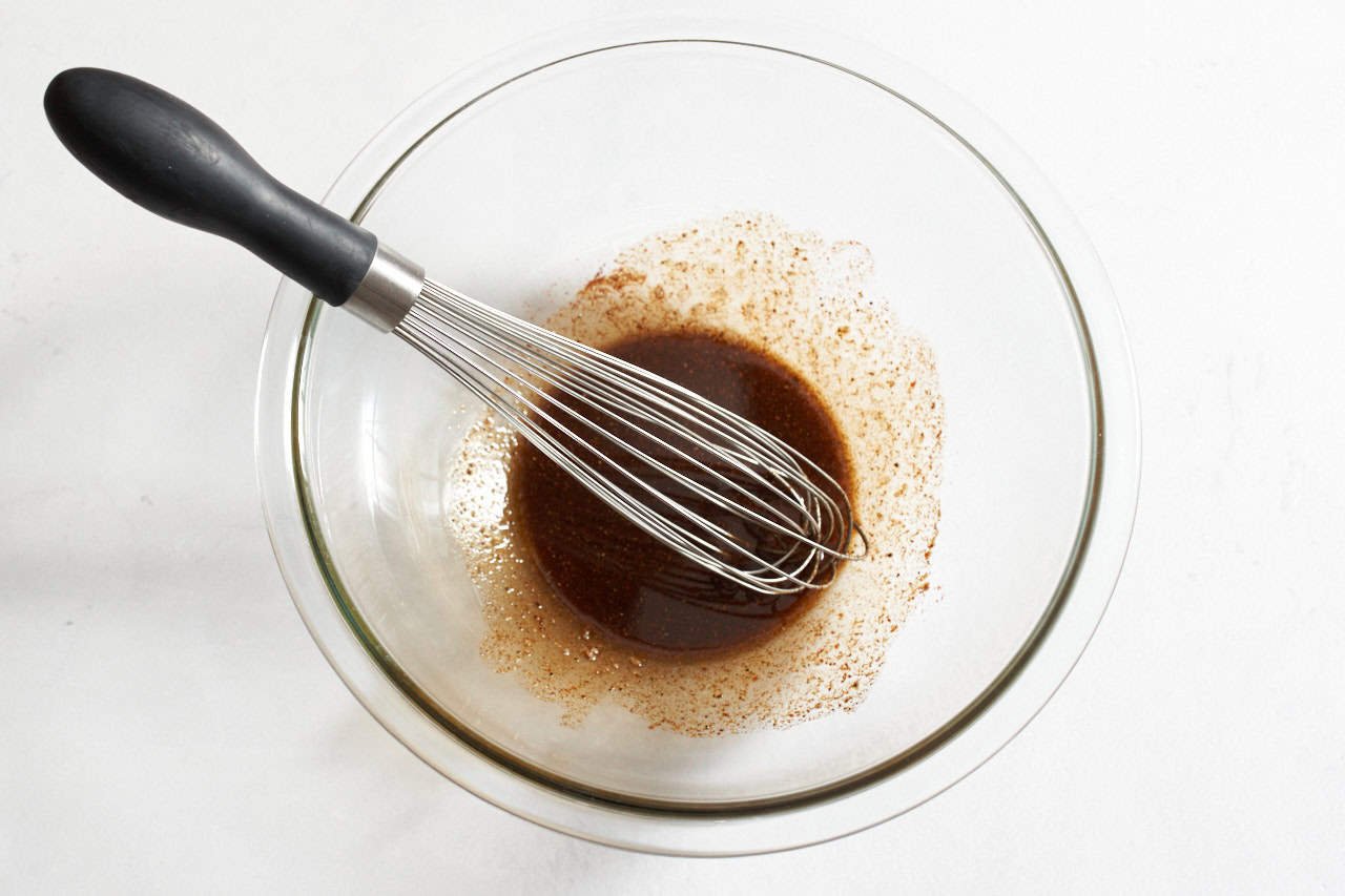 Olive oil and dried spices mixed together in glass bowl with a whisk in it.