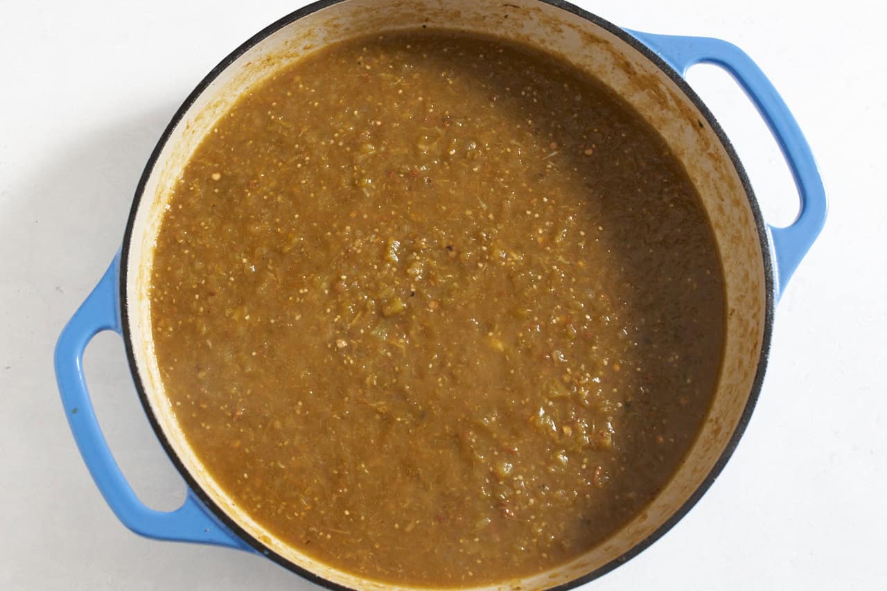 Salsa verde with green chilis in a pan with blue handles.