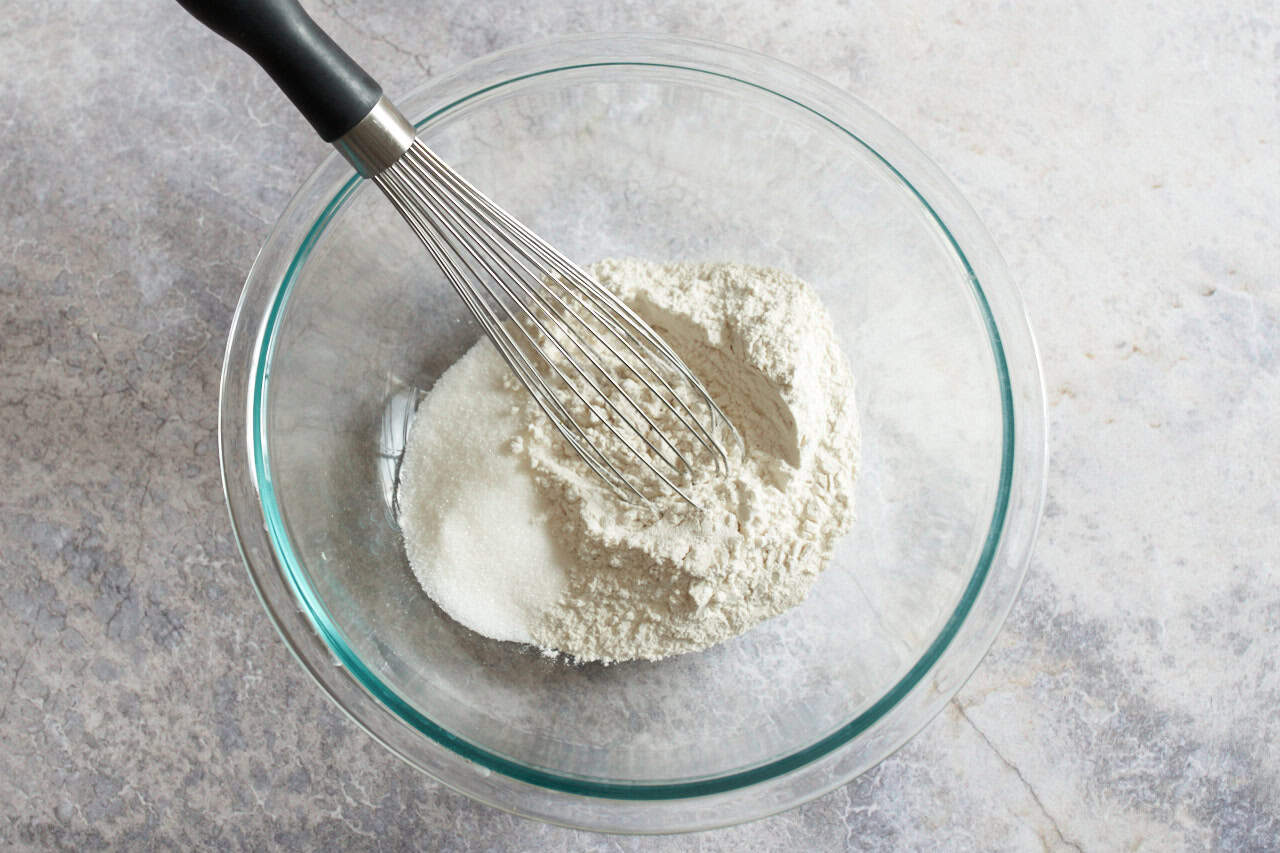 A glass bowl of flour and sugar with a whisk in it.