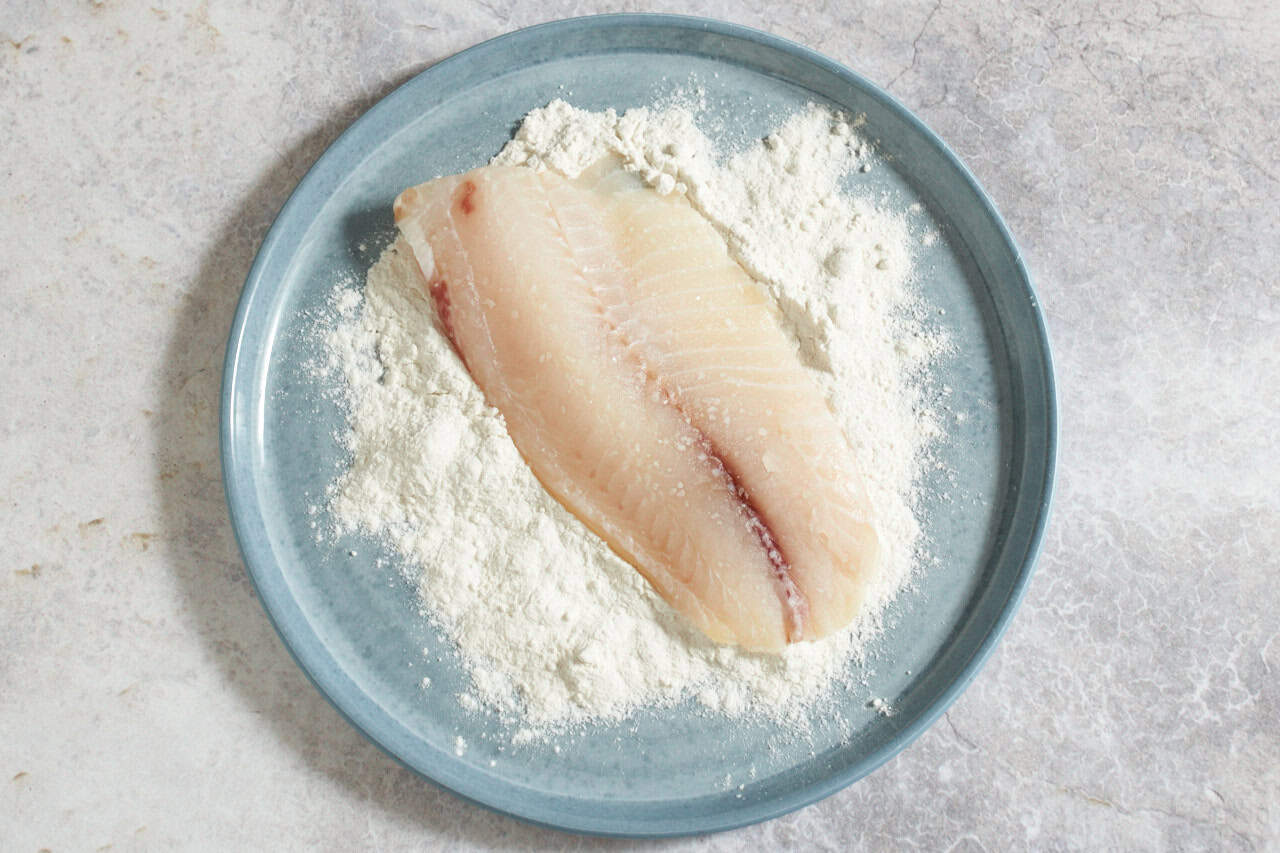 A fish fillet in flour on a blue plate.