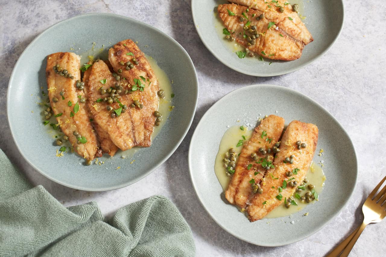 Three plates of fish with lemon butter sauce on top, garnished with fresh parsley.