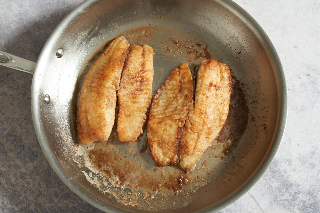 Pan seared fish fillets that are golden brown in a skillet.