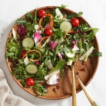 An insalata mista (Italian mixed salad) on a wooden plate with gold serving utensils.