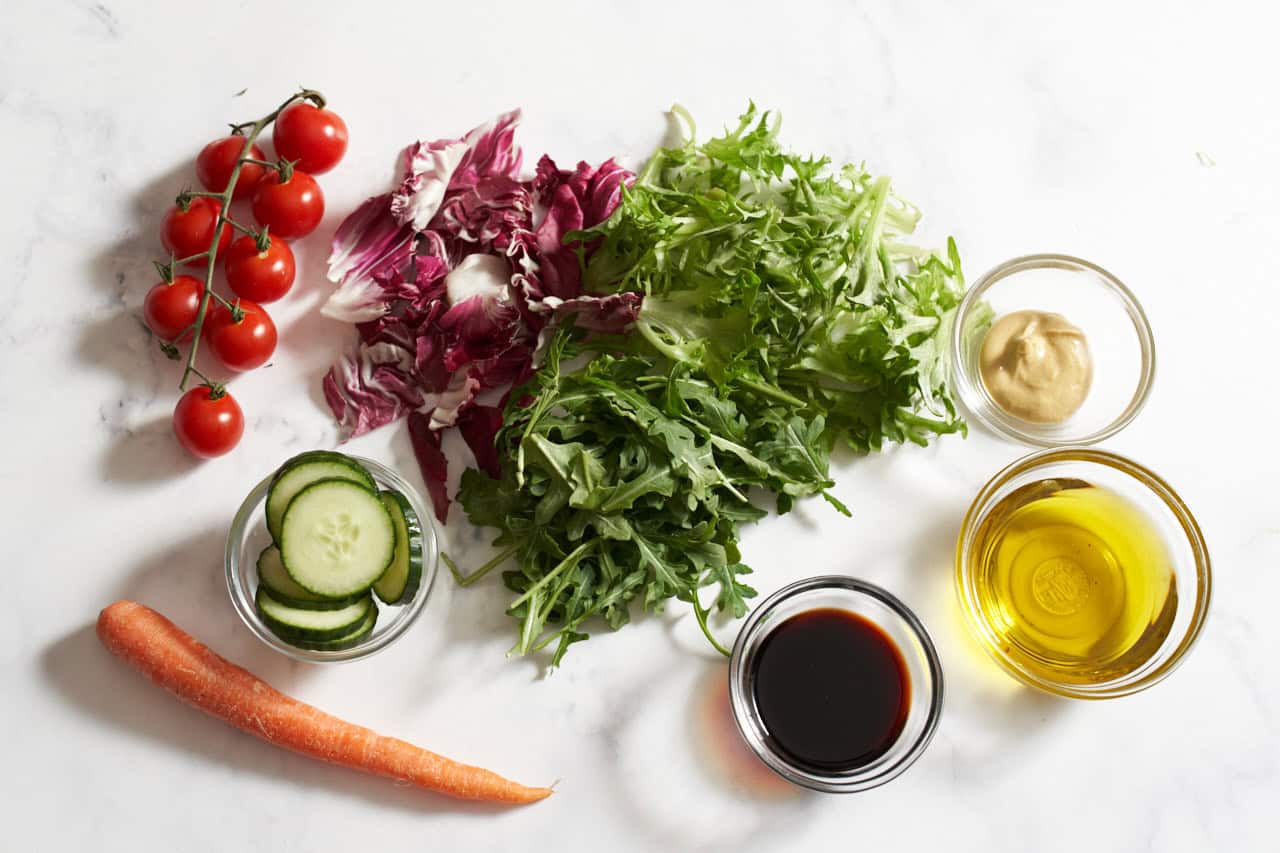 Fresh arugula, radicchio, escarole, a carrot, some cherry tomatoes, and small bowls of sliced cucumbers, balsamic vinegar, olive oil, and dijon mustard.