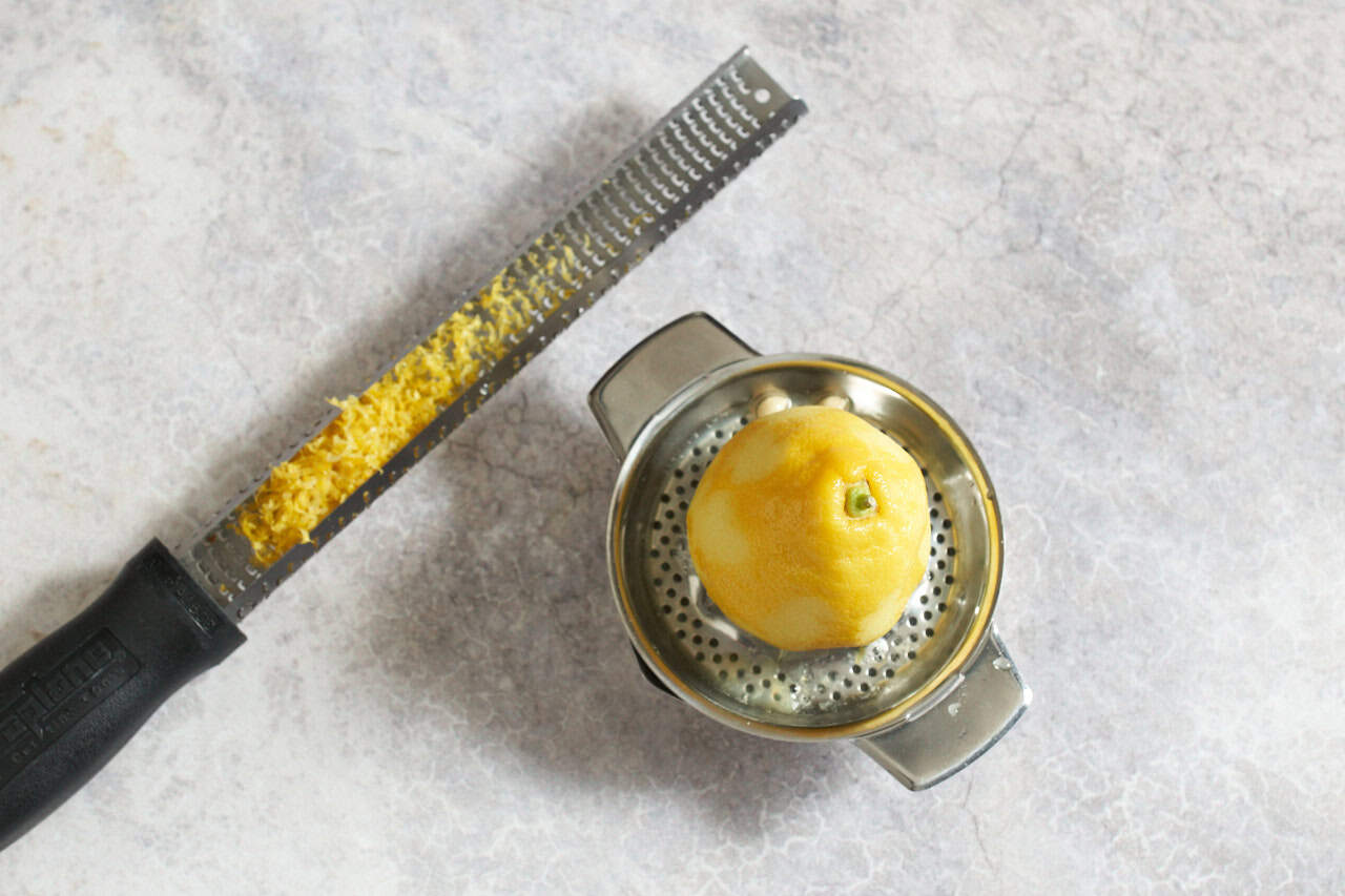 A microplane grater with lemon zest next to a juicer with half a lemon.