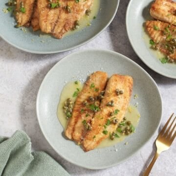 Three plates of fish with lemon butter sauce on top, garnished with fresh parsley.