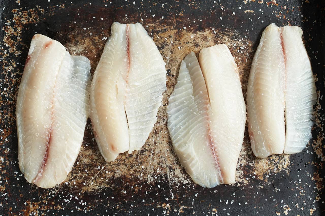 Fish fillets on a sheet pan seasoned with kosher salt.