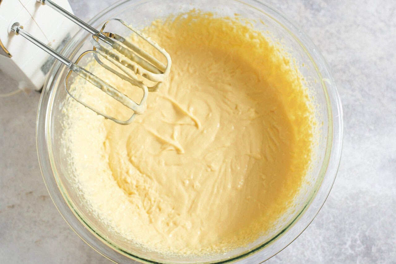 A hand mixer over a bowl containing mango pulp that has been blended with mascarpone cheese and sugar.
