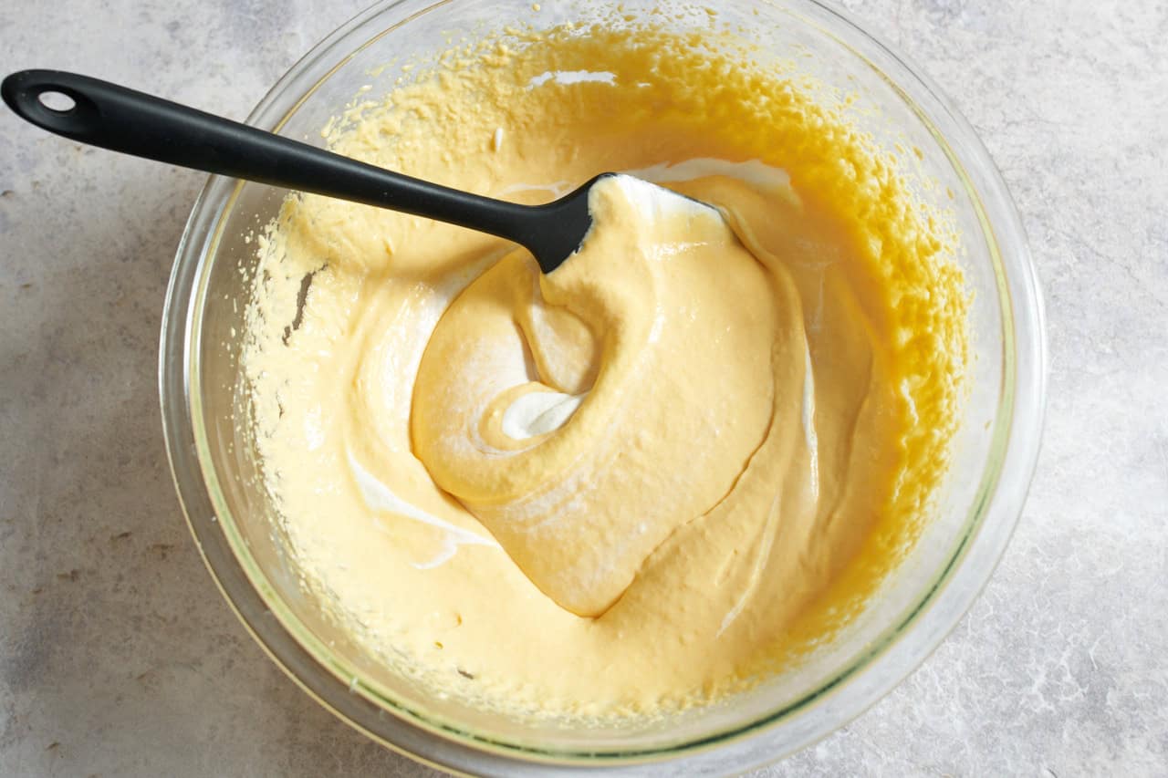 A large bowl with whipped cream being folded into a creamy mango mixture.