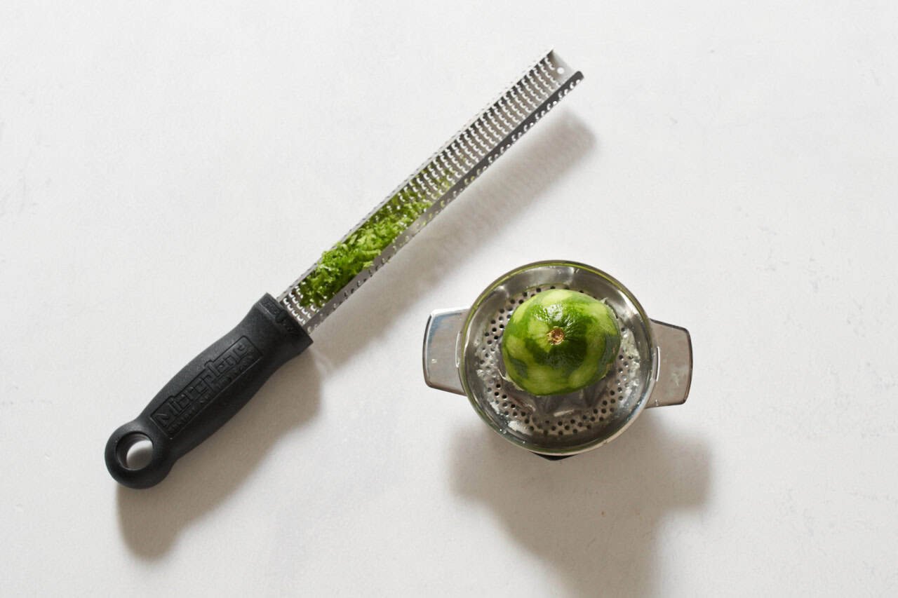 A microplane grater with lime zest next to a juicer with half a lime on it.