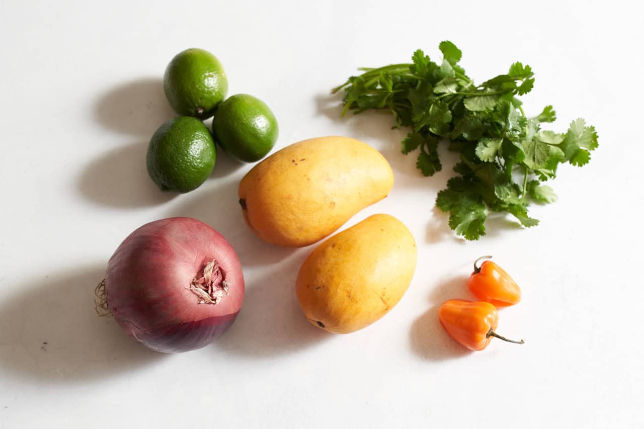 Three limes, two mangoes, fresh cilantro, a habanero pepper, and a red onion.