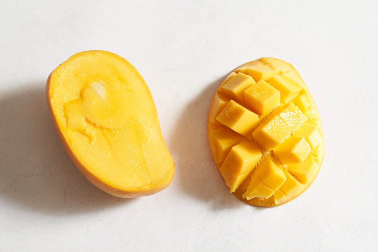 A mango cut in half, the portion on the right has been cross-hatched into cubes.