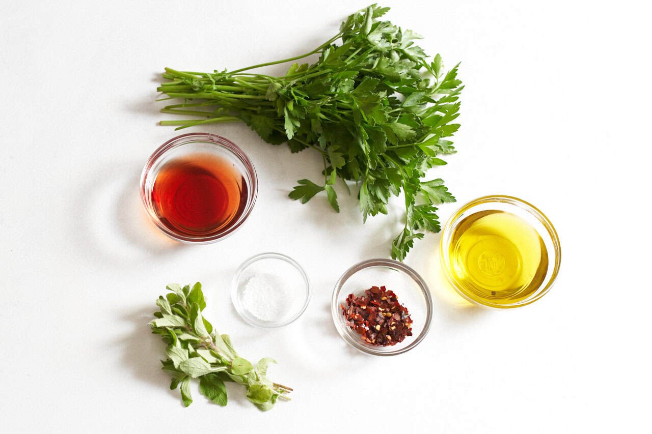 Fresh parsley, fresh oregano, and three small glass bowls of olive oil, red wine vinegar, salt, and crushed red pepper flakes.