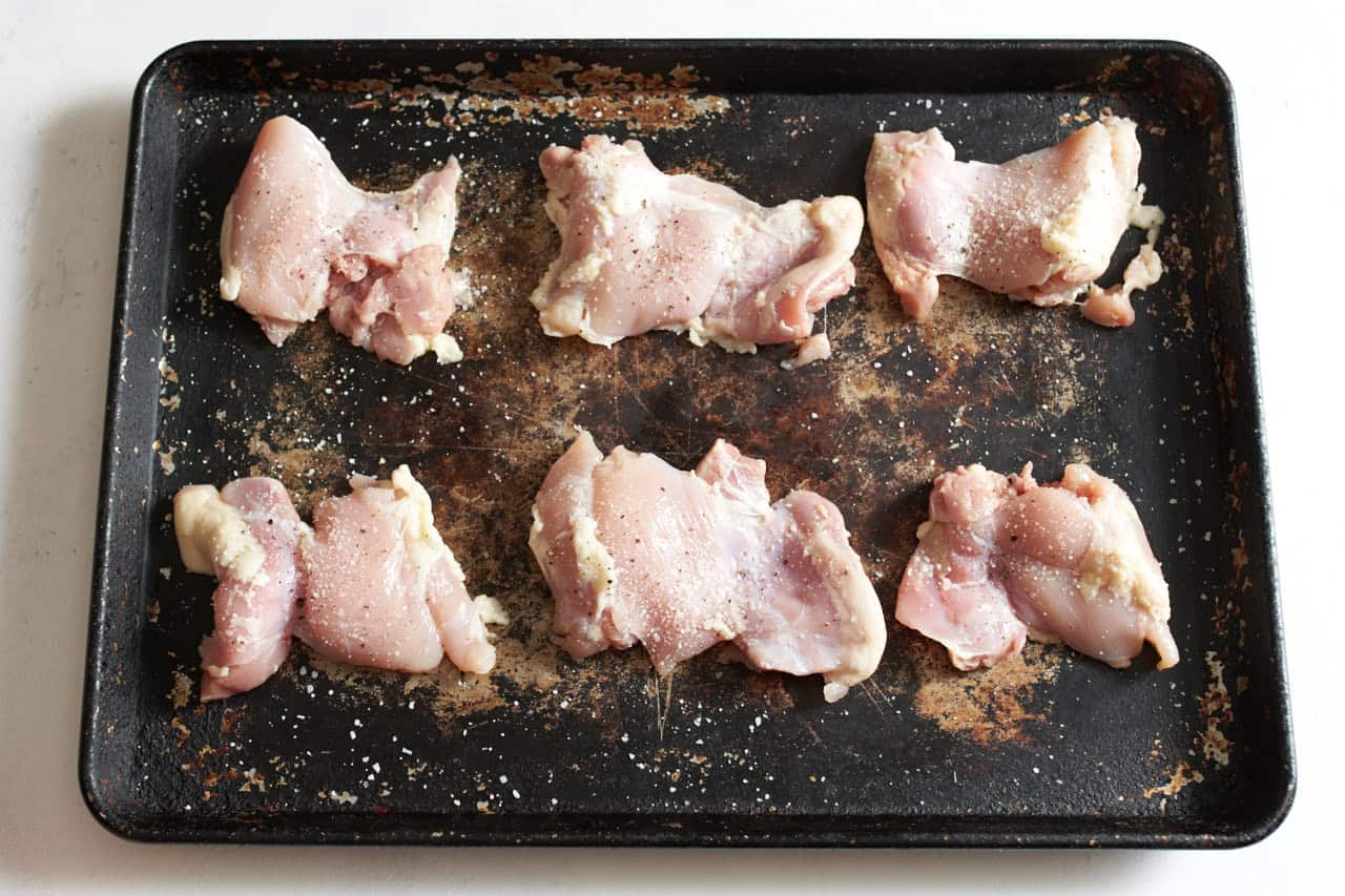 Chicken thighs seasoned with salt and pepper on a sheet pan.