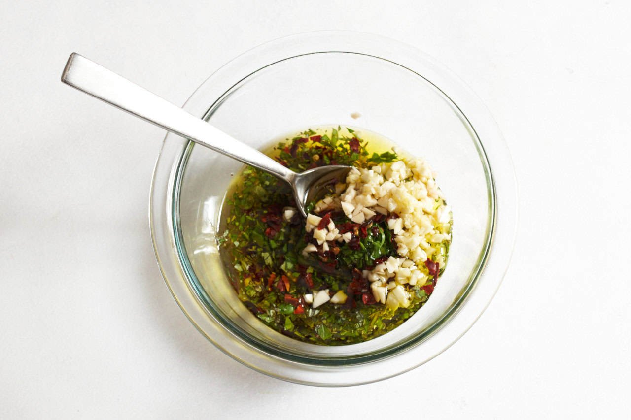 A spoon in a bowl of ingredients for chimichurri sauce, ready to be combined.