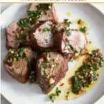 Slices of grilled pork tenderloin with chimichurri sauce on a white plate.
