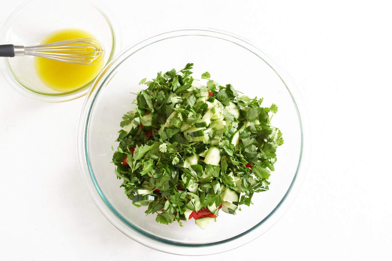 A bowl of lemon dressing next to a larger bowl of salad ingredients.