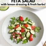 Two plates of cucumber, tomato, and feta salad, two green glasses are in the upper left, a gold fork is in the lower right.