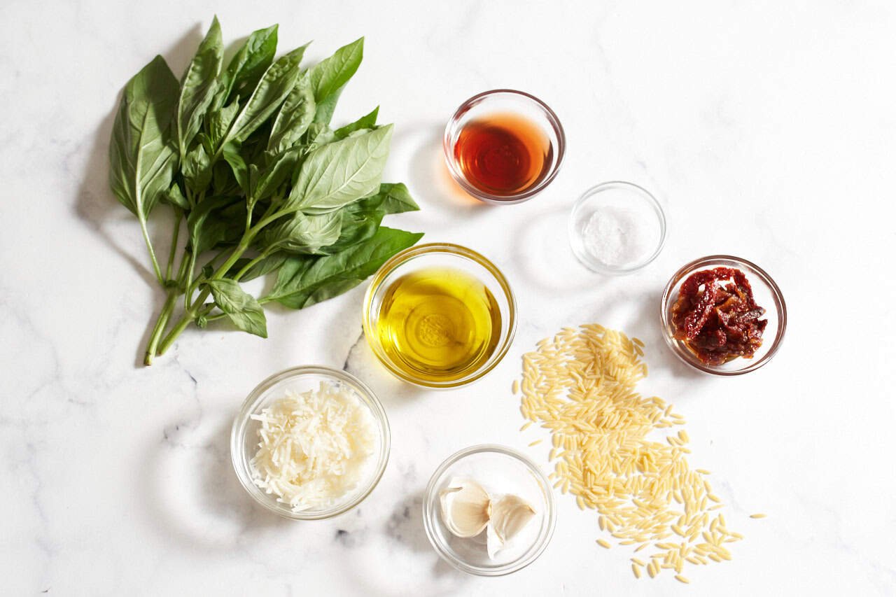 A bunch of fresh basil, orzo pasta, and small bowls of garlic, grated parmesan cheese, olive oil, red wine vinegar, sun dried tomatoes, and salt.