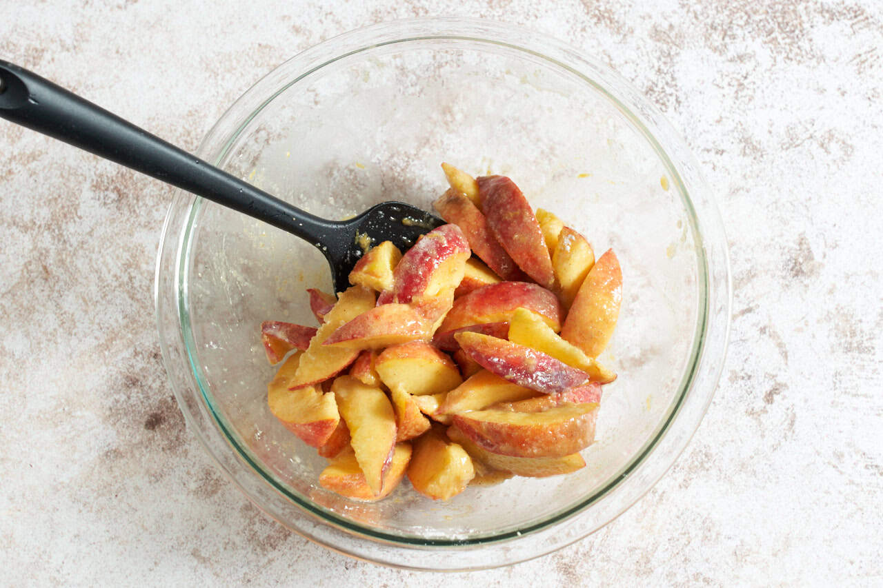 A bowl of sliced peaches coated in brown sugar, cardamom, and corn starch.