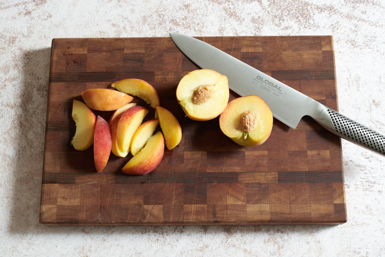 A knife on a wooden cutting board with sliced peaches.