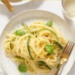 Zucchini mascarpone pasta on a white plate garnished with fresh basil leaves, a gold fork is on the right side of the plate.