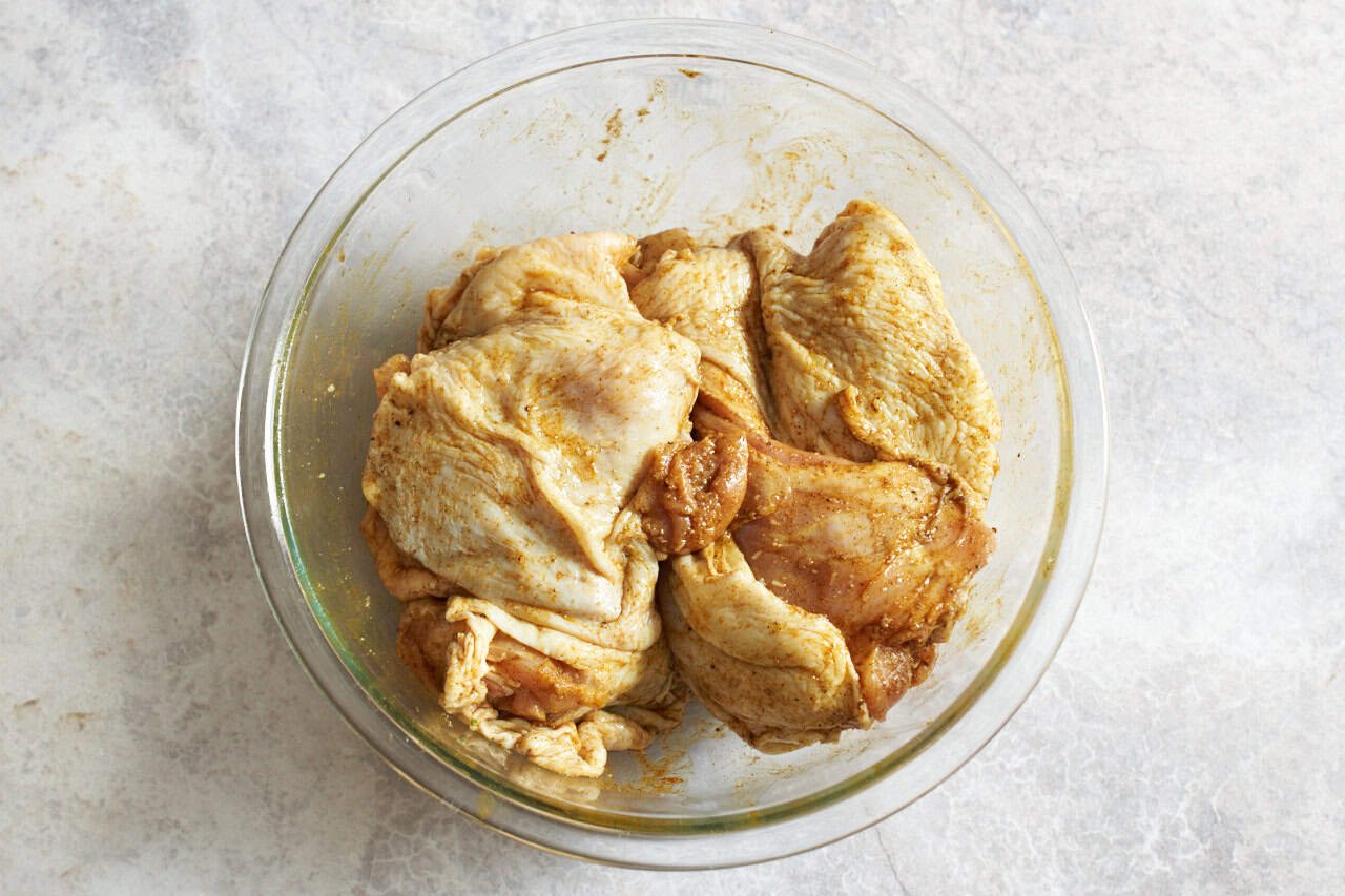 Chicken thighs coated in spices in a glass bowl.