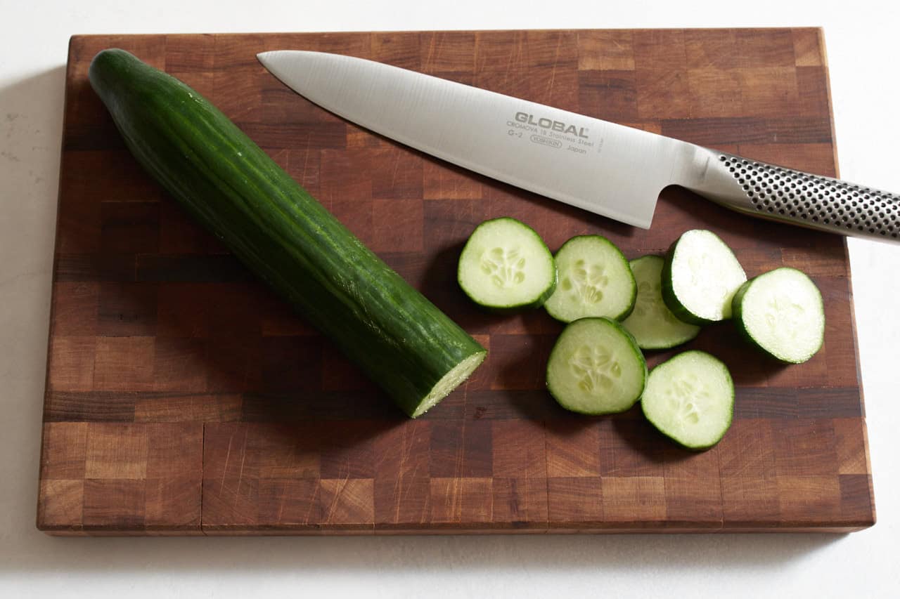 An English cucumber and slices of cucumber on a wooden cutting board with a knife.