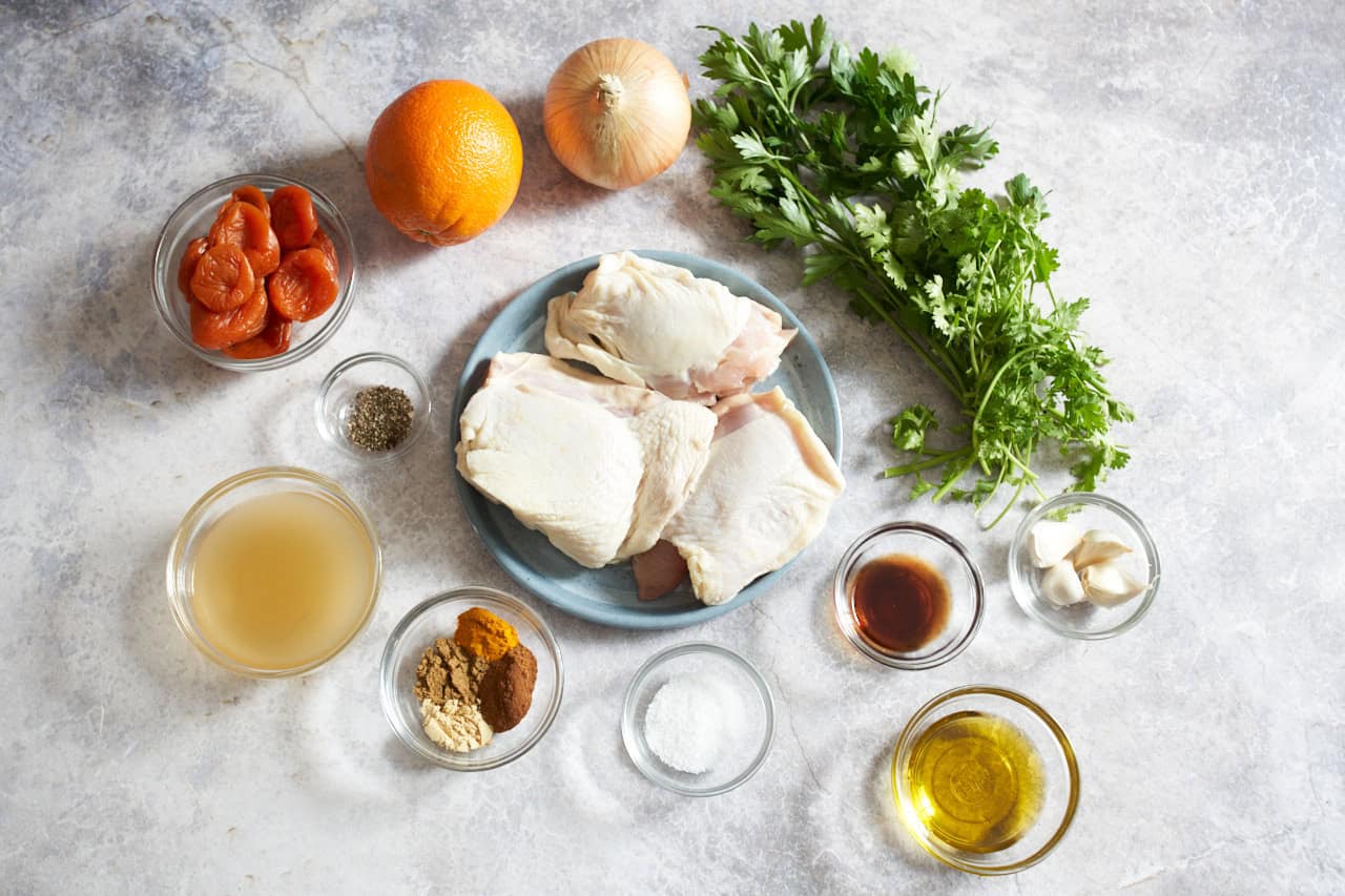 An onion, an orange, bunches of fresh parsley and cilantro, small bowls of spices, vinegar, olive oil, garlic, and chicken stock.