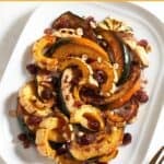 A platter of roasted winter squash topped with cranberry agrodolce and hazelnuts, a gold fork is on the right.